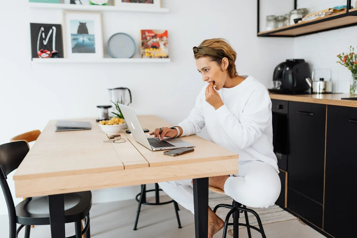 A woman at a kitchen counter working something out on a laptop