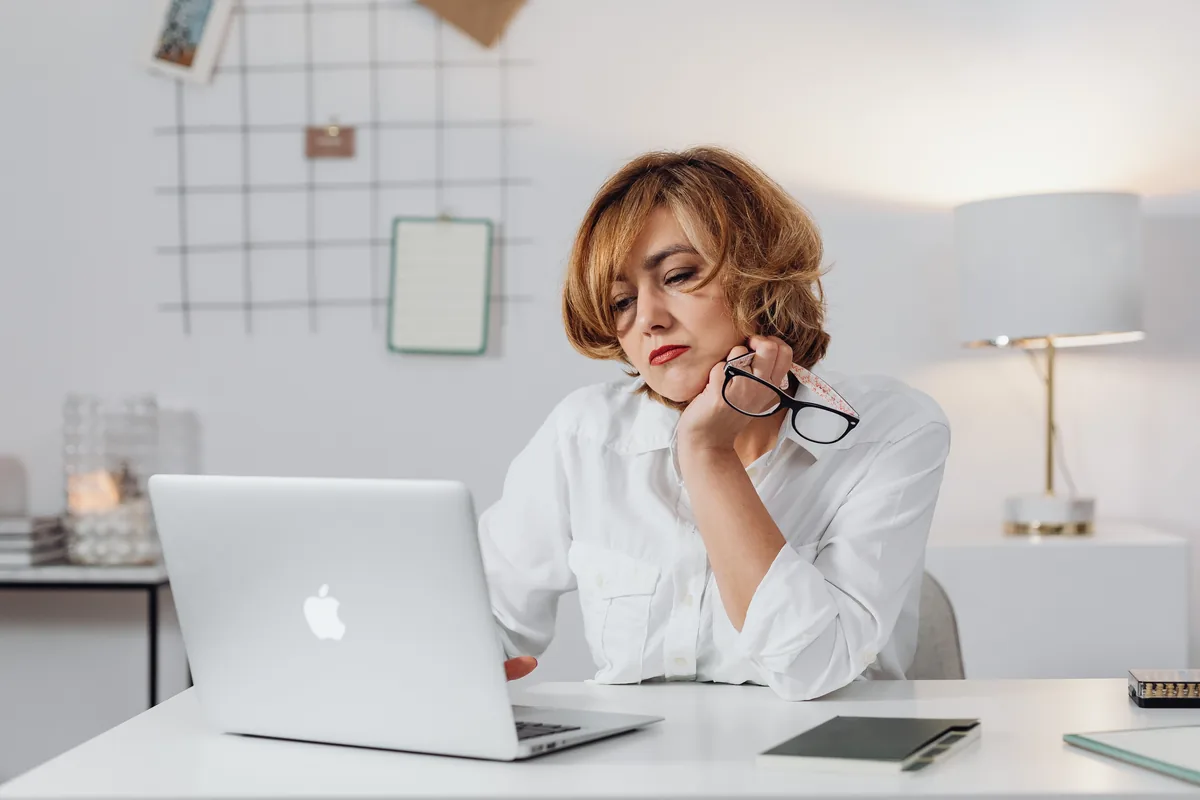 A woman checking something carefully on her laptop, glasses in hand