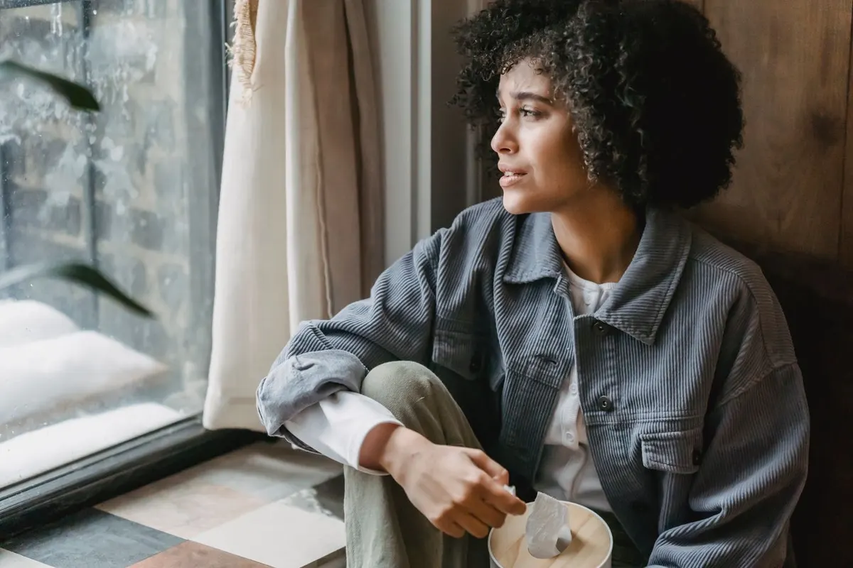 A woman sitting by a window, looking thoughtful