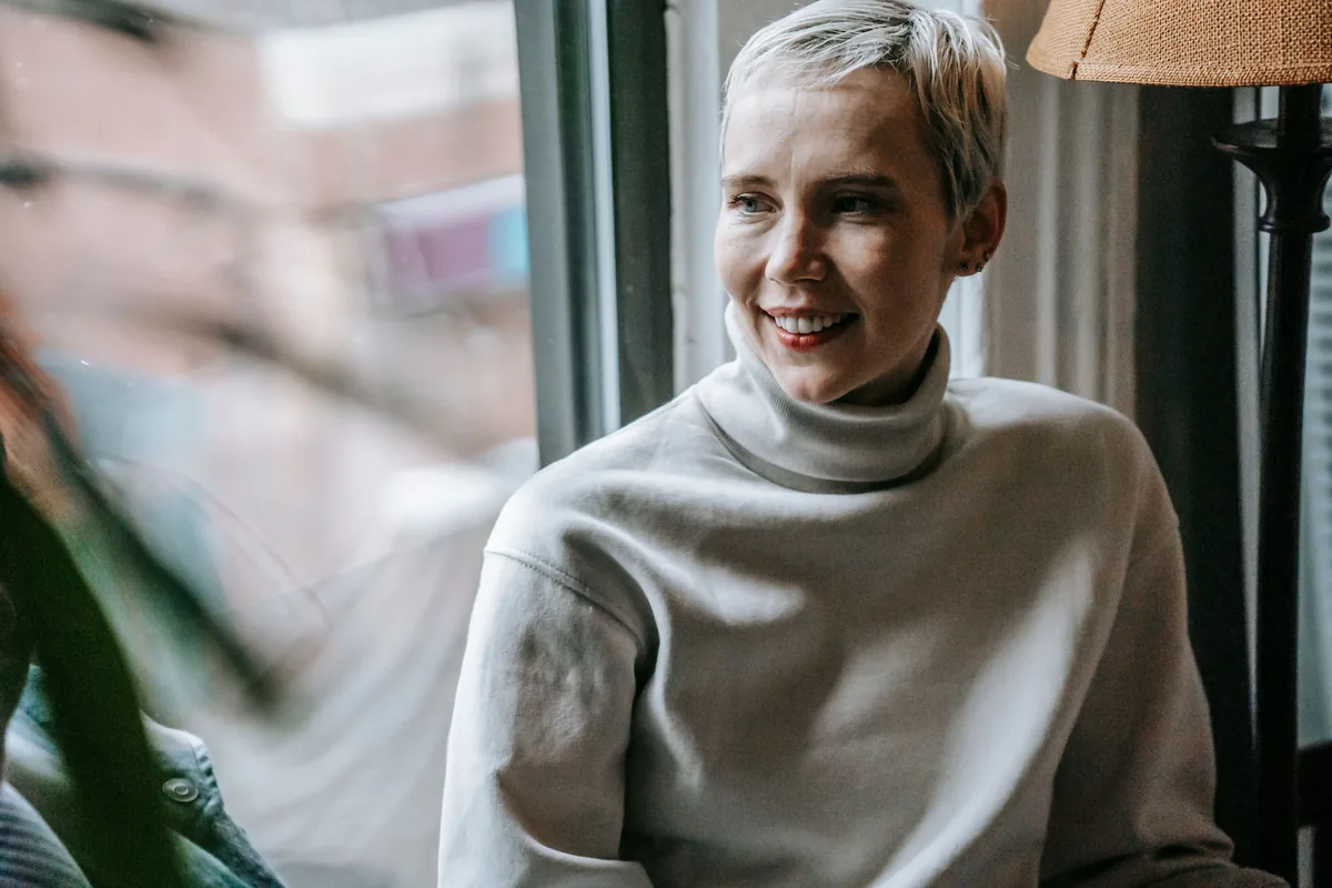 A woman smiling as she talks, sitting by a window