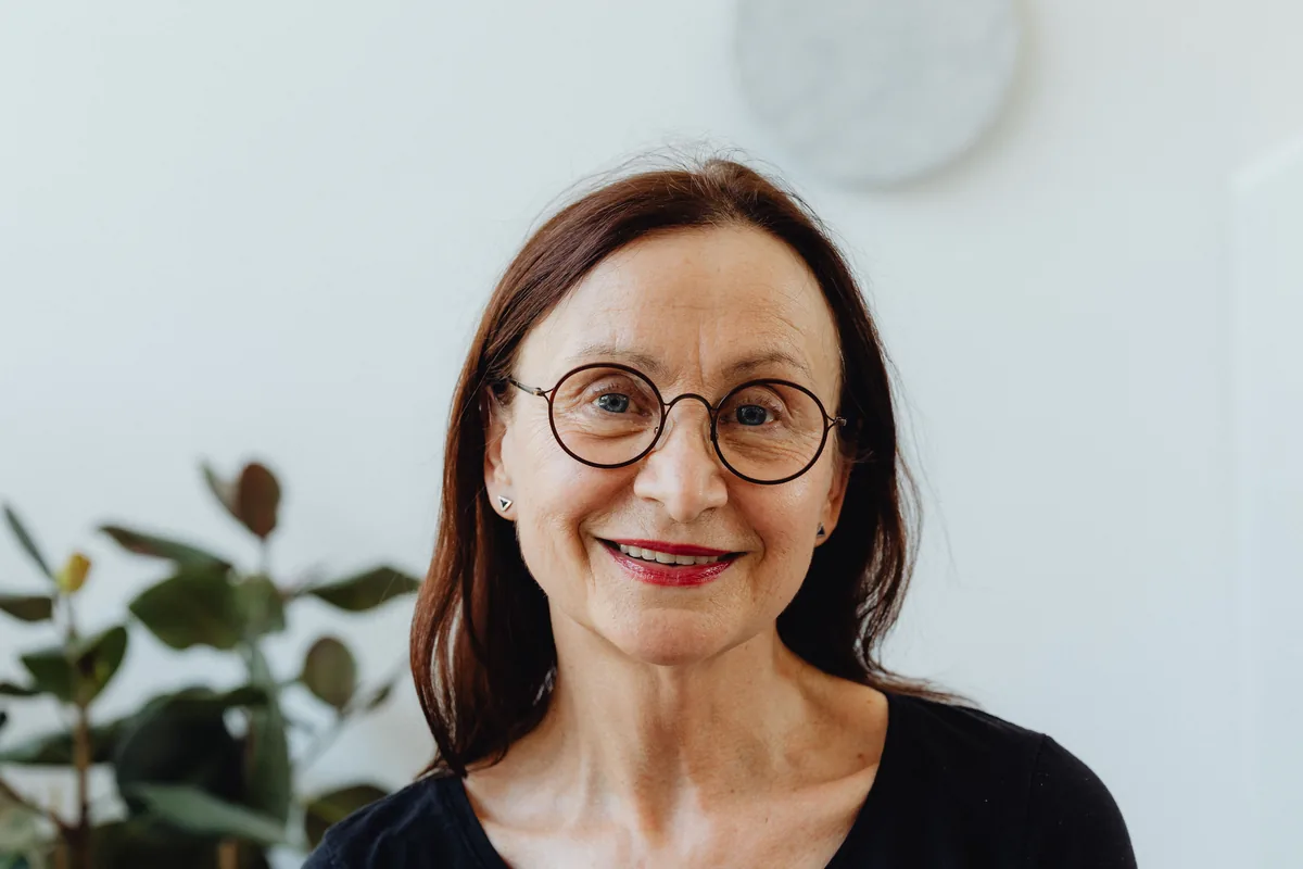A woman with glasses smiling, in a bright room