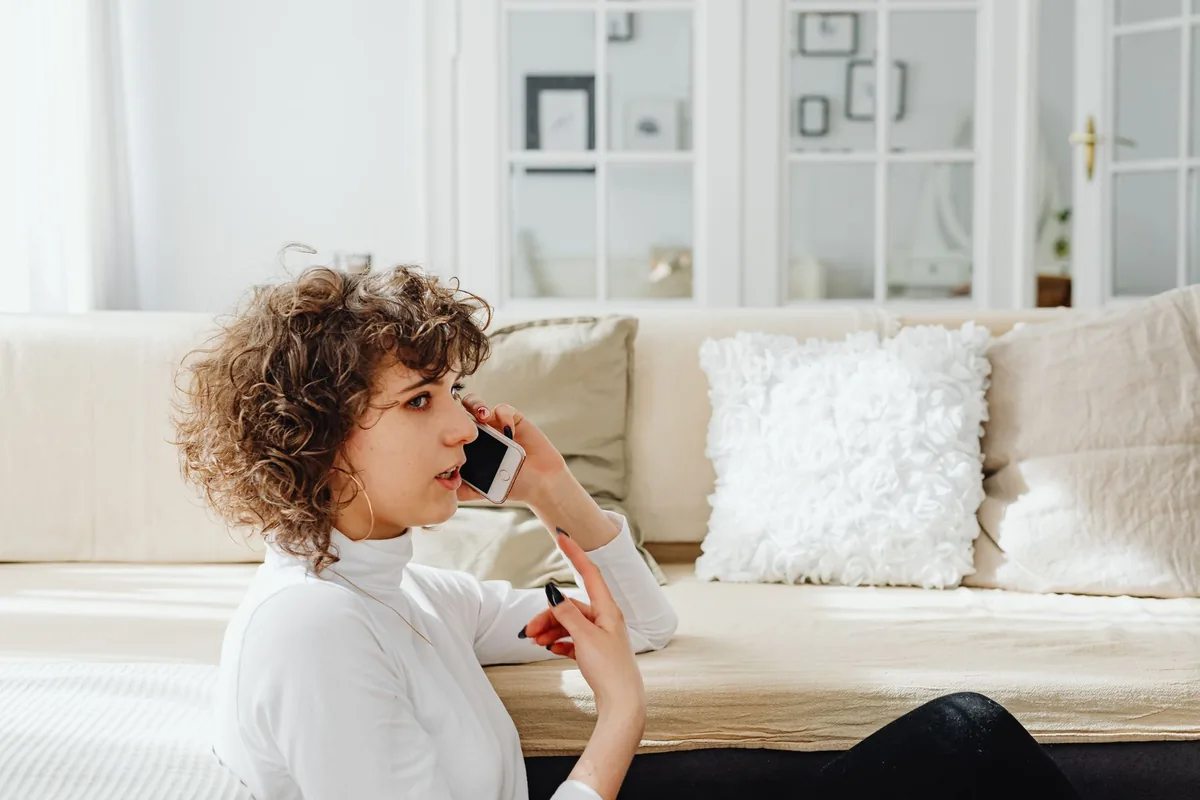 A woman sitting in a bright room, talking on her phone