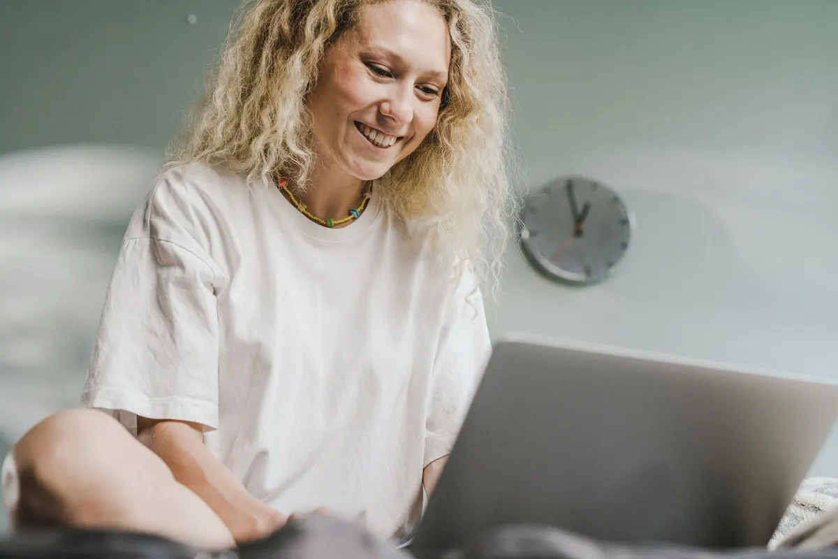 A woman in her forties smiling as she uses a laptop at home