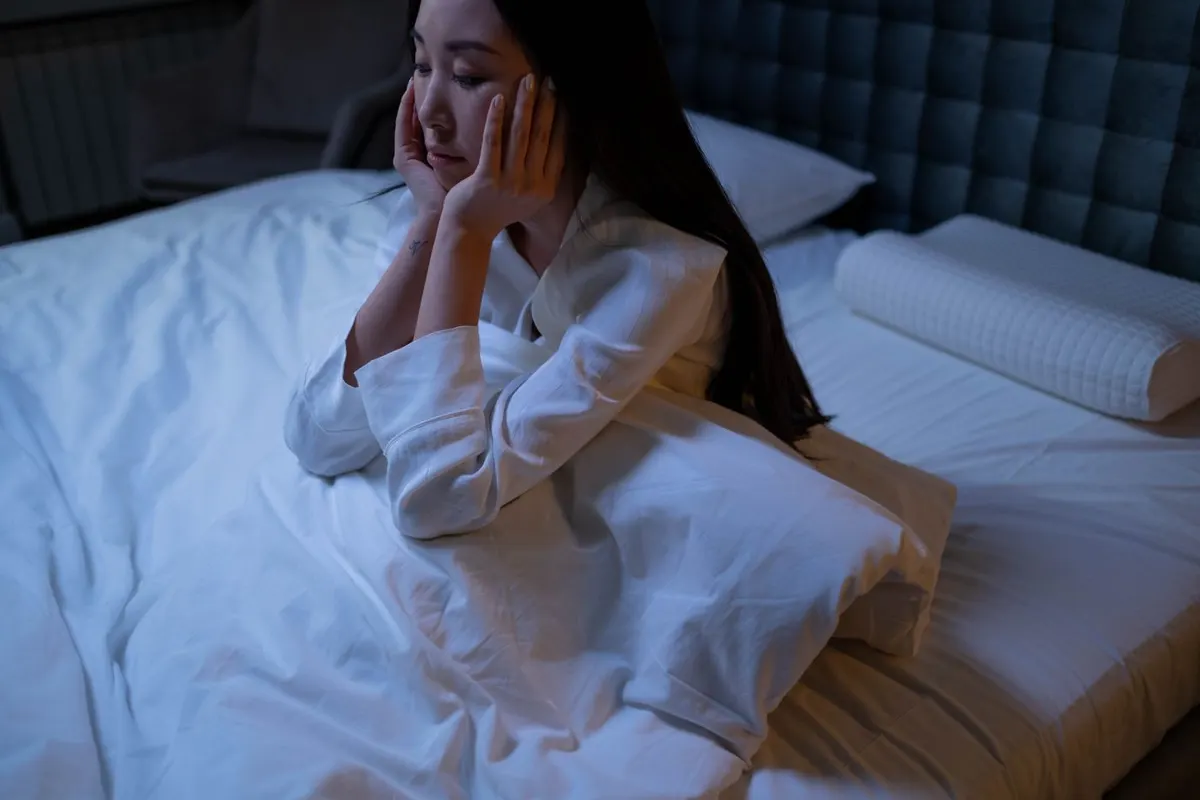 A woman awake on the edge of her bed at night