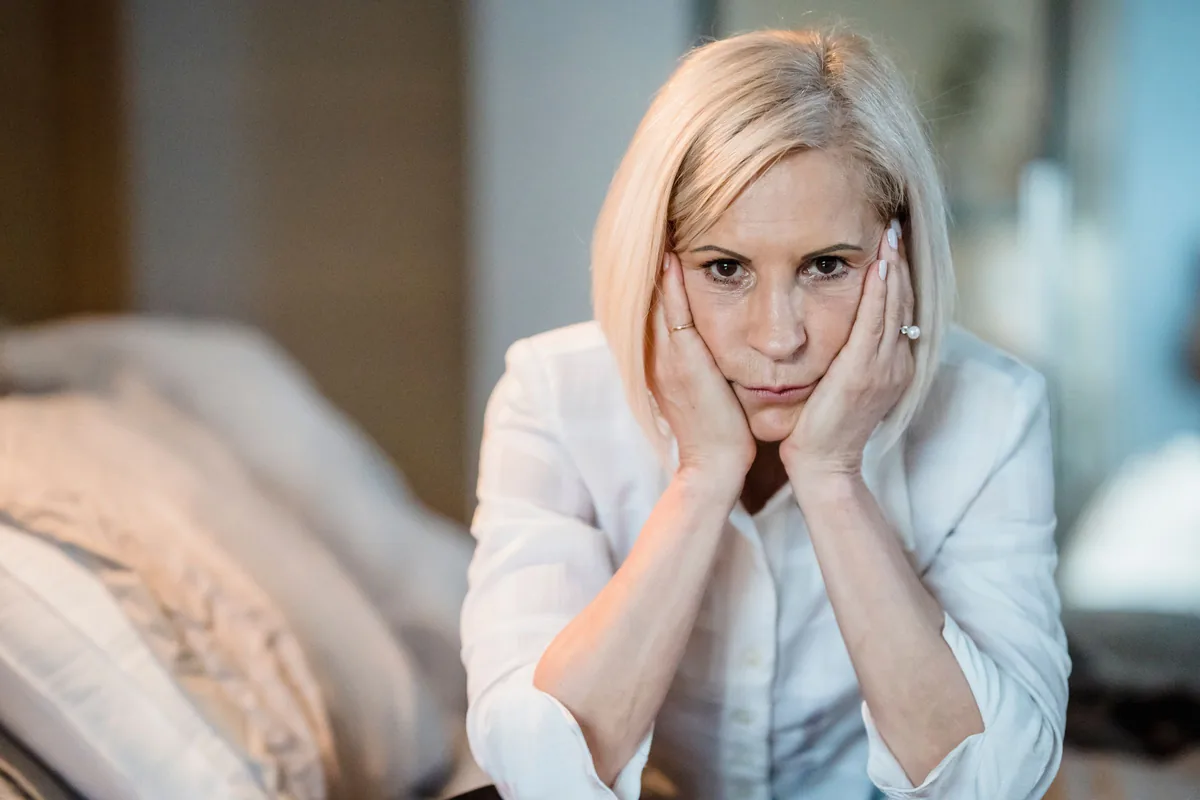 A woman in her fifties resting her chin on her hands, looking straight ahead