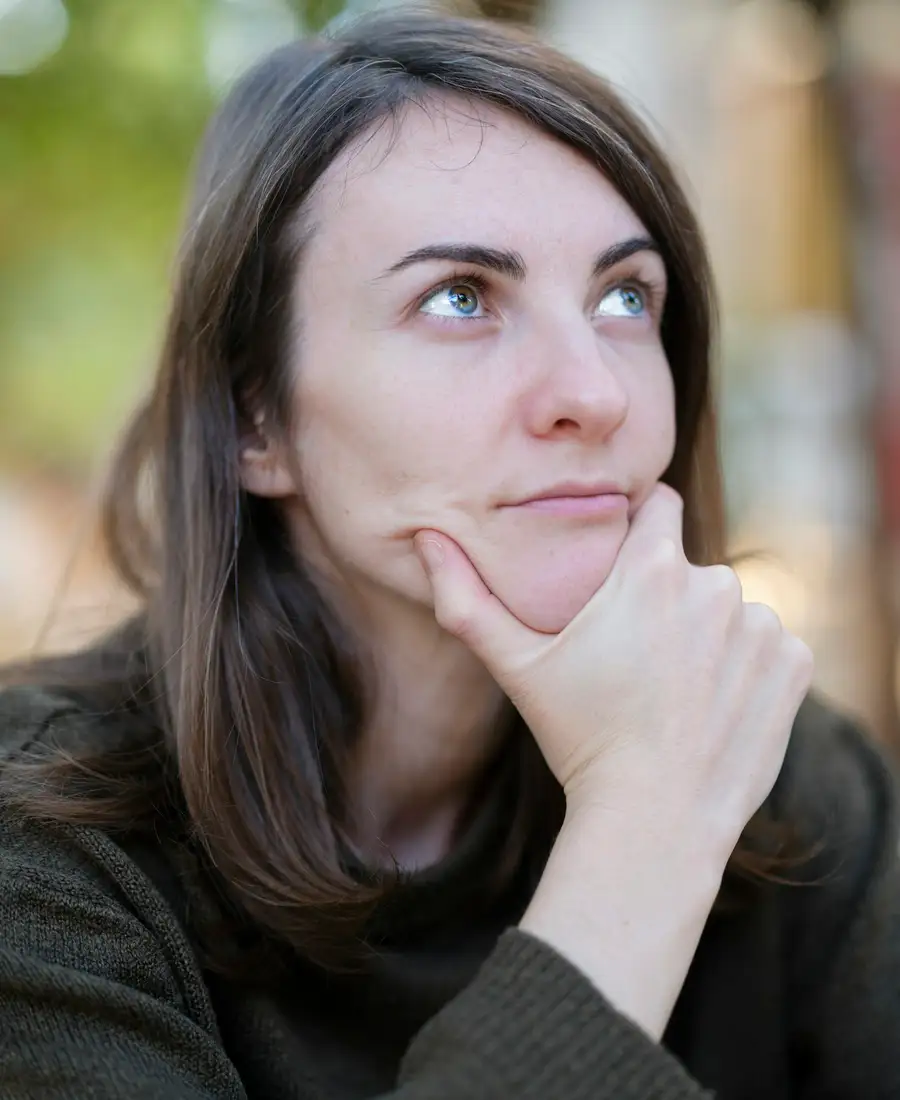 A woman in her forties pausing to think, hand resting against her chin